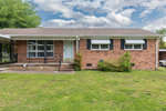 Single-story brick suburban house with a covered front porch and white door, under a partly cloudy sky.
