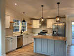 A modern kitchen with white cabinets, stainless steel appliances, a gray island, and pendant lighting.