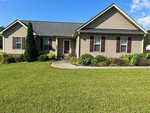 A single-story beige house with dark red shutters, a covered front porch, and a landscaped front yard with a curved walkway.