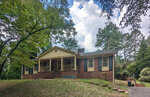 Single-story brick house with a front porch, surrounded by trees, under a cloudy sky.