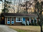 A single-story brick house with blue shutters and a front porch displaying an american flag at dusk.