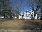 A single-story white house with red trim and a small front porch, situated in a neighborhood with bare trees and clear skies.