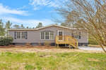 A single-story manufactured home with gray siding and white trim, featuring a small wooden porch with stairs on a grassy lot.