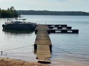A pontoon boat moored to a wooden dock on a calm body of water with surrounding trees.