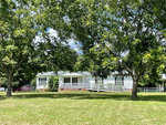 A single-story house with white siding, a front deck, and surrounded by green trees under a clear sky.