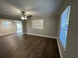 A spacious, empty room with laminate flooring, white walls, a ceiling fan, and large windows allowing natural light in.