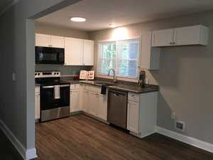 A modern kitchen with stainless steel appliances, white cabinetry, and wood-look flooring.