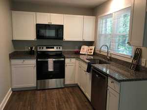 A modern kitchen interior with white cabinetry, granite countertops, stainless steel appliances, and a window above the sink.