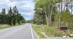 A two-lane road surrounded by trees and vegetation with a few vehicles in the distance and a mailbox in the foreground.