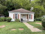 A small white house with red trim and a gabled roof, featuring a front door with a wheelchair ramp.
