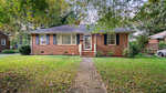 A quaint brick single-story house with a pitched roof and a front lawn, featuring a concrete pathway leading to the entrance.