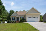 A single-story suburban house with a two-car garage and a well-manicured lawn on a sunny day.