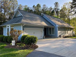A single-story house with a gray roof, white siding, and an attached garage, set against a backdrop of trees under a clear sky.