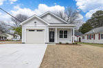 A single-story white house with black trim, featuring a front-facing garage and a gabled entrance.