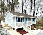 A small blue single-story house with white trim and a front porch, located in a wooded area.