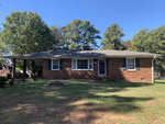 Single-story brick house with a shallow-pitched roof and front lawn, situated under a clear blue sky.