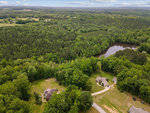 Aerial view of a rural landscape featuring a dense forest area with a small lake and a few scattered houses connected by roads.