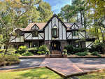 A tudor-style house surrounded by trees with a well-manicured lawn and a brick pathway leading to the front entrance.