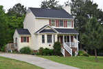 A two-story suburban house with beige siding, white trim, a covered front porch, and a landscaped yard.