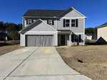 A two-story house with white siding and a double garage, featuring a concrete driveway and a neatly trimmed lawn under a clear blue sky.