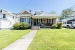 A single-story house with a covered porch and a front lawn, under clear skies on a sunny day.