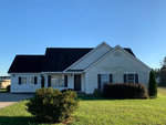 A single-story, white suburban house with a black roof and a front lawn under a clear blue sky.