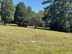 A red suv parked in the grass near a brick house with a hay bale in the foreground and tall trees in the background on a sunny day.