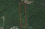 An aerial view of a rectangular piece of land outlined in red, surrounded by a dense forested area.