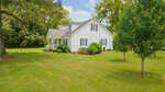 A white single-story house with a gabled roof, surrounded by a well-manicured lawn and a few trees under a partly cloudy sky.