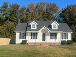 A single-story white house at 64 Allen Road, Henderson NC, with a central entrance flanked by two windows, a gabled roof, and surrounded by a lawn with trees in the background.