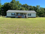 A single-story house with white siding and a front porch, located at 629 Townsville Landing Road, Henderson NC, is set on a large lawn with trees in the background and clear blue skies above