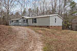 A single-story beige modular home with a small front porch and brick underpinning, situated on a sloped grassy terrain at 360 Spring Lane, Henderson NC. A gravel driveway leads to the