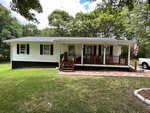 A single-story white house at 624 Doctor Finch Road, Henderson NC, with a covered front porch and an American flag displayed on a flagpole, parked next to which is a white pickup truck in