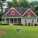 A red and white suburban house at 321 Hedrick Drive, Henderson NC, with a gabled roof, featuring a front porch and manicured bushes, set against a backdrop of green trees and a