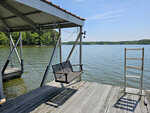A wooden dock with a swinging bench under a roof, overlooking a calm lake on a clear day at 306 Waters Edge Loop, Henderson NC.