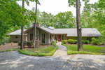 Single-story residential home at 2111 Coleman Place, Henderson NC with a sloped roof and brick facade surrounded by mature trees, featuring a walkway leading to a red front door with sidelights and