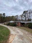 A single-story brick residential building located at 2990 Stagecoach Road, Henderson NC, with a sloped roof, featuring an adjacent driveway and surrounded by trees under an overcast sky.