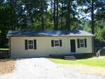 A single-story beige house with a dark roof and two windows, located at 139 Southern Avenue, Henderson NC, is situated in a sunny area with trees in the background.