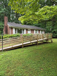A single-story house with a brick chimney and a large wooden ramp leading up to the front door, located at 605 Roanoke Avenue, Henderson NC, surrounded by green lawn and foliage.