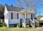 A small, single-story white house with purple shutters and a front porch under a clear blue sky, located at 7917 N NC 39 Highway, Henderson NC.