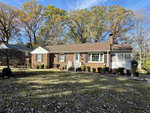 A single-story brick house at 1510 Oakdale Circle, Henderson NC, with white trim, featuring a central white door with side panels, flanked by two large windows, and a chimney on