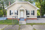 A single-story tan house at 350 N Clark Street, Henderson NC, with white trim and a small front porch, enclosed by a low chain-link fence, with a concrete walkway leading to the