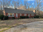 A single-story red brick house with white-trimmed windows, a shingled roof, and a chimney at 933 Daniel Harris Road, Henderson NC, surrounded by bare trees and a lawn with