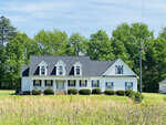 A white single-story house with a gabled roof and four dormer windows situates amid a grassy field under a clear sky at 324 Kelly Road, Henderson NC.