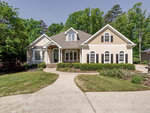 A single-story beige house with a gray roof, white trim, and an arched entryway at 129 Us Grant Court, Henderson NC, surrounded by trees under a clear blue sky. A concrete