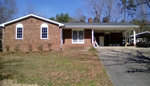 A single-story brick house with an attached carport on a sunny day in Henderson, NC, featuring a front lawn and a paved driveway.
