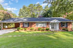 Single-story brick house with a white front door and attached carport, located at 1516 Cypress Drive, Henderson NC, surrounded by trees and a well-maintained lawn with a stepping stone pathway