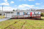 Single-story manufactured home with an attached garage and a red wooden front deck under a clear sky, located at 1395 Tollie Weldon Road, Henderson NC.