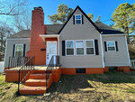 A two-story house at 715 Highland Avenue, Henderson NC, with gray siding and orange accents, featuring a red-brick chimney and staircase.