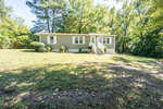 A single-story house with gray siding is positioned among trees on 109 Old Watkins Road, Henderson NC, featuring white stairs leading to a side entrance, on a sunny day with shadows cast across the lawn